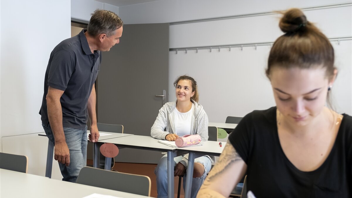 Ein Lehrer unterhält sich im Klassenzimmer mit einer Schülerin.